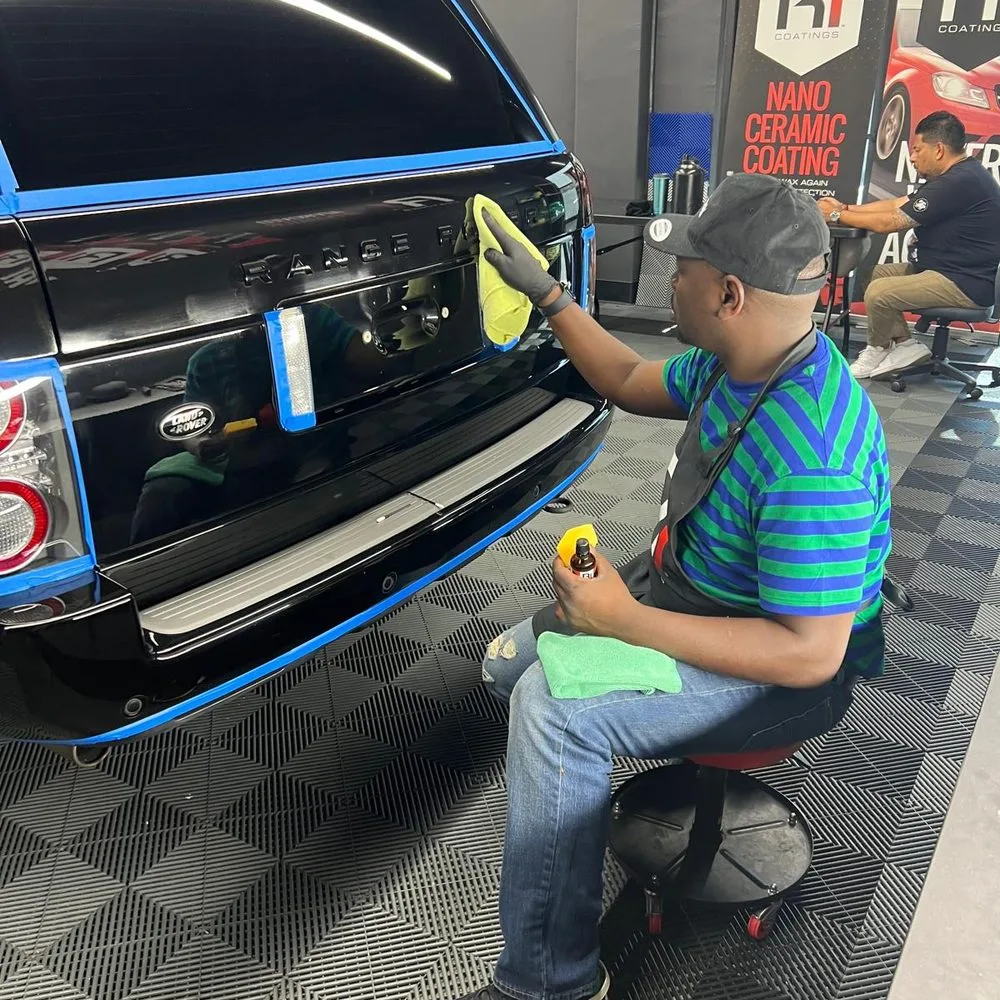 A Baby Blanket technician wiping ceramic coating into the rear panel of a black Range Rover inside the shop's coating bay
