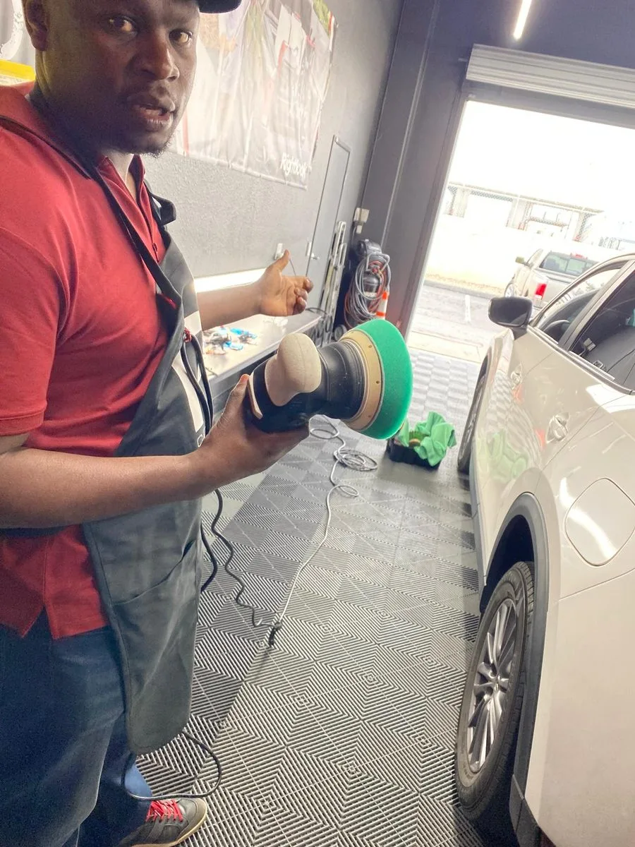 A technician holding a rotary polisher alongside a white car during paint correction